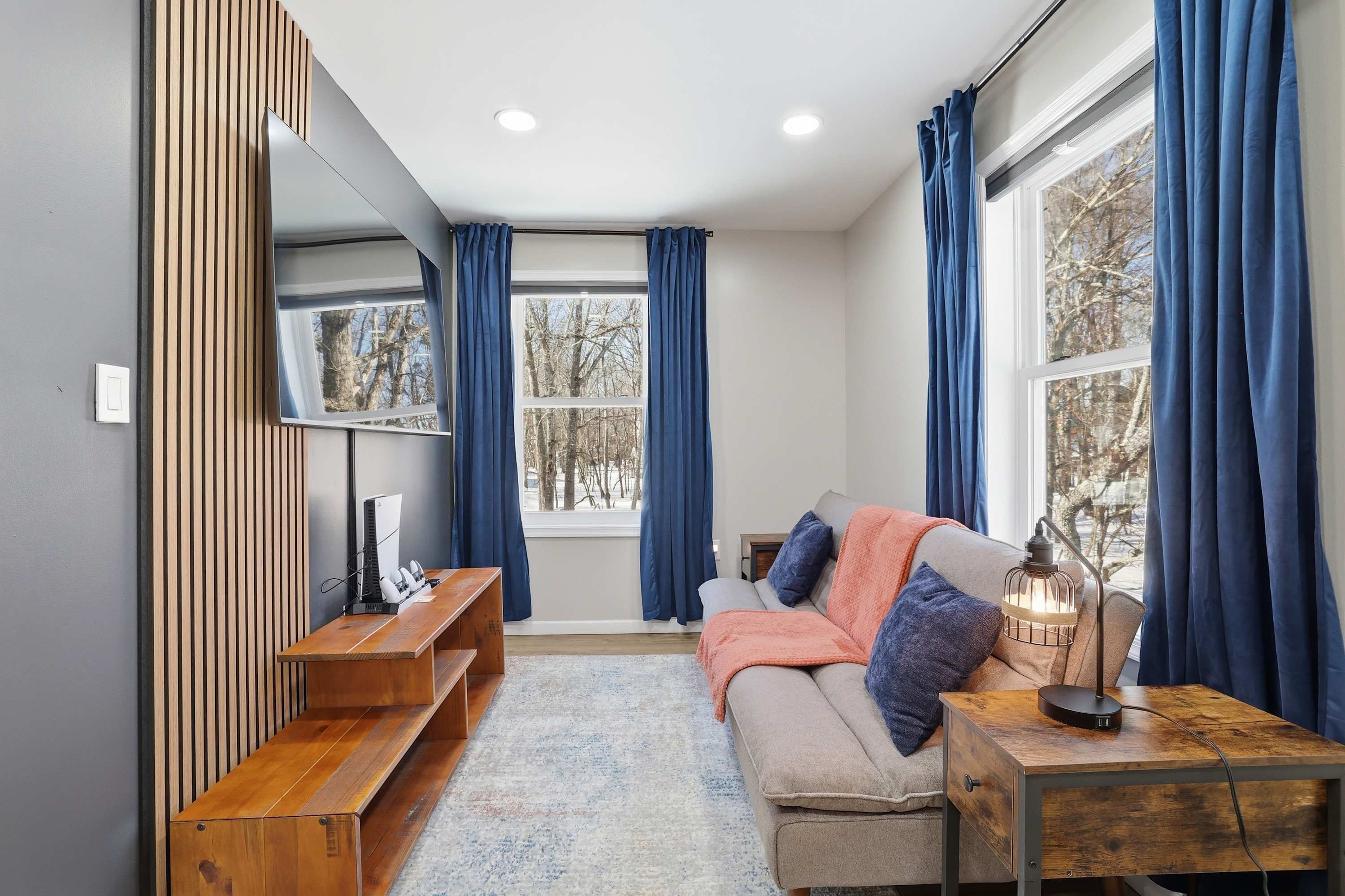 A modern living room with a sofa, a wooden bench, a side table, a lamp, and a large mirror.
