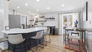 A modern kitchen with a central island, bar stools, and a dining area with a table and chairs. - Amenity-filled Retreat by Jfbb-pickleball-gameroom (Albrightsville)