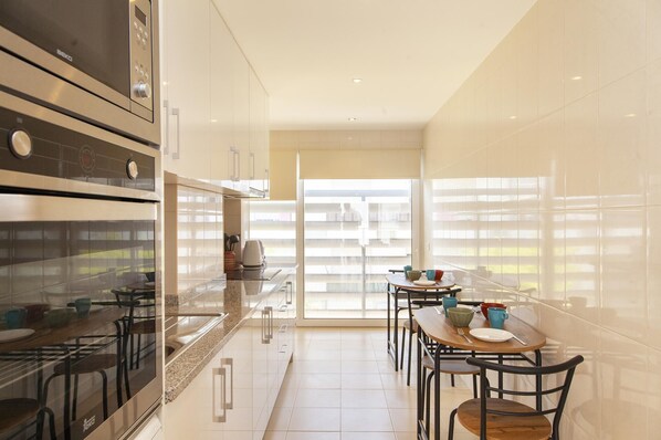 A modern kitchen with a dining area, featuring a large window, stainless steel appliances, and a minimalist design. - Y 03 - Bedroom 3 in Trindade Sun Guesthouse (Lagos)