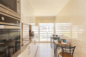 A modern kitchen with a dining area, featuring a large window, stainless steel appliances, and a minimalist design.