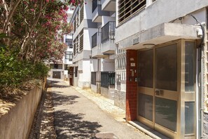 Rua estreita com edifícios, uma entrada com portão e um edifício com porta de vidro grande.