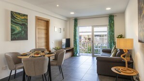 A modern living room with a dining area, a sofa, a TV, and a balcony with curtains. - B74 - Baluarte Holiday Flat in Lagos (Lagos)