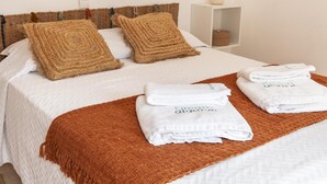 A neatly made bed with two brown woven pillows, a white bedspread, and a brown throw blanket. There are three folded white towels with text on them. - B40 - Levante 2 Bedroom Apartment in Lagos (Lagos)