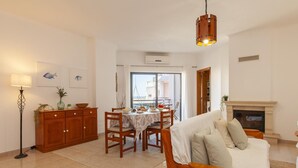 A living room with a sofa, a dining area with a table and chairs, a fireplace, and a balcony with a view. - B40 - Levante 2 Bedroom Apartment in Lagos (Lagos)