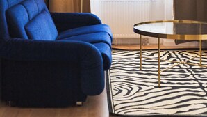 Une pièce avec un canapé bleu, une table ronde en verre, un tapis à motifs zébrés et un lampadaire.
