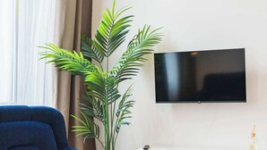 Un salon avec un canapé bleu, un téléviseur fixé au mur, une console blanche et une grande plante en pot.