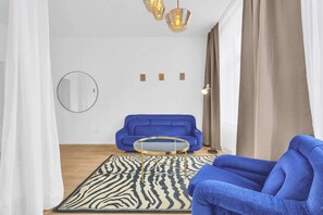 A living room with a blue sofa, a round coffee table, a zebra-patterned rug, a round mirror, and a modern chandelier. - Trendy Apartment in Centrum 2 (Bratislava - Old Town)