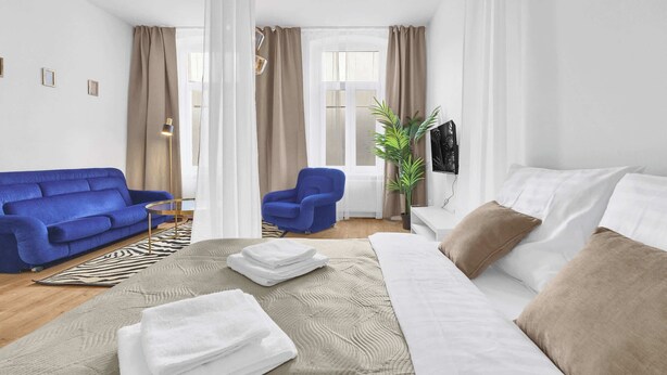 Une chambre d’hôtel moderne avec un lit, un canapé bleu, un fauteuil, une télévision et une plante.