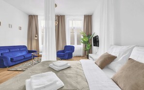Una habitación de hotel moderna con una cama, un sofá azul, una silla, un televisor y una planta.