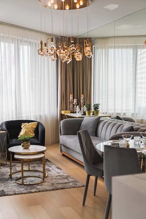 A modern living room with a sofa, chairs, a round table, and a decorative chandelier. - Skypark's Luxury Suite II with Prime View (Bratislava - Old Town)