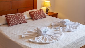 Un letto rifatto con cuscini decorati, un asciugamano arrotolato e una lampada su un comodino.