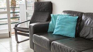 Ein schwarzes Ledersofa mit Türkis-Kissen, ein schwarzer Ledersessel und eine Glastür zu einem Balkon mit einer Palme.