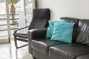 En svart lädersoffa med turkosa kuddar, en svart läderfåtölj och en glasdörr som leder ut till en balkong med en palm.