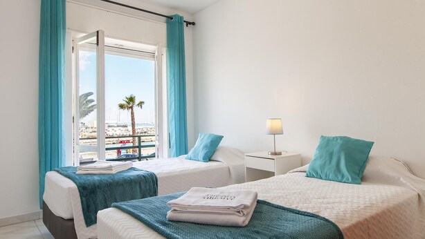 Ein Hotelzimmer mit zwei Betten, einem Balkon, einer Lampe und Blick auf den Hafen.