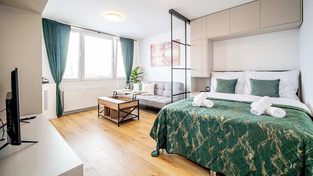 A modern hotel room with a bed, a desk, a TV, and a window with curtains.