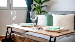 A dining table with two wine glasses and plates, a sofa, and a plant in the background.