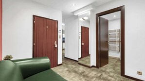 Una habitación de hotel con un sofá verde, puertas de madera, un espejo y suelo de baldosas.