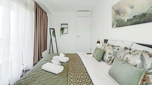 A hotel room with a bed, a bedside table, a wall-mounted air conditioner, a framed picture, and a window with curtains. - Urban White Oasis in Centre (Bratislava - Old Town)
