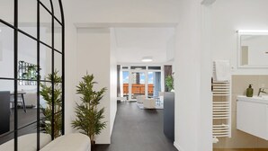 A modern interior with a hallway leading to a dining area, a white reception desk, and a view of the outside. - Urban White Oasis in Centre (Bratislava - Old Town)