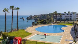 A pool with a red umbrella, palm trees, and a view of the sea and buildings. - A73 - Iberlagos Studio Flat (Lagos)