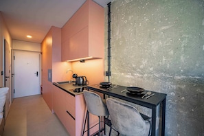 A compact kitchen with a single island, a sink, and a stove. There are two chairs and a small table with a kettle and a frying pan.