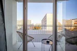 A balcony with two chairs and a small table, overlooking a parking lot and buildings.