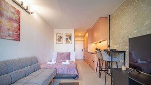 A compact hotel room with a sofa, a bed, a TV, a desk, and a chair. - Cozy Hideaway Studio with Balcony (Košice)