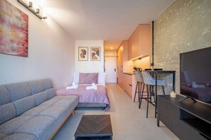 A compact hotel room with a sofa, a bed, a TV, a desk, and a chair.