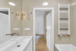 Ein modernes Badezimmer mit einer großen Badewanne, einem weißen Handtuchhalter und einem Spiegel.