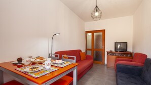 Ein gemütlicher Wohnbereich mit Esstisch, roten Stühlen, einer Couch, einem Fernseher und einer dekorativen Leuchte.