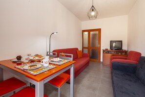 Ein gemütlicher Wohnbereich mit Esstisch, roten Stühlen, einer Couch, einem Fernseher und einer dekorativen Leuchte.