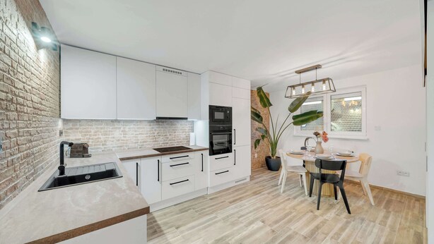 Una cucina moderna con mobili bianchi, una parete decorata con mattoni, un lavello e un'area pranzo con tavolo e sedie.