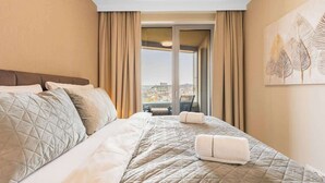 Ein Hotelzimmer mit Bett, Vorhängen, Blick durch ein Fenster und einem Wandbild.