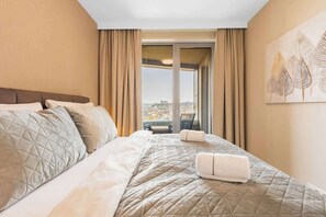 A hotel room with a bed, curtains, a view through a window, and a wall art piece. - Skypark's Royal Castle View (Bratislava - Old Town)
