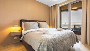 Ein Hotelzimmer mit Bett, Nachttisch, Lampe, einem Fenster mit Vorhängen und Blick auf die Stadt.