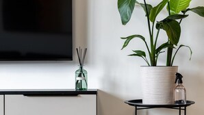 A modern living room with a flat-screen TV mounted on the wall, a white cabinet below, a round black coffee table, a potted plant, and a small glass bottle on the table.