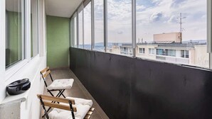 A balcony with a view of buildings, a black wall, and two wooden chairs.