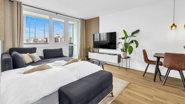A modern hotel room with a large bed, a TV, a desk, and a dining area.