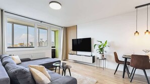 A modern living room with a sofa, TV, dining table, chairs, and a large window.