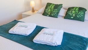 Ein ordentlich bezogenes Bett mit zwei gefalteten Handtüchern, einer grünen Tagesdecke und zwei Kissen mit grünem Blattmuster.