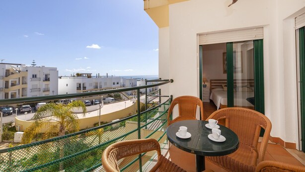 Ein Balkon mit Korbstühlen, einem Tisch und Blick auf das Meer und die Gebäude.