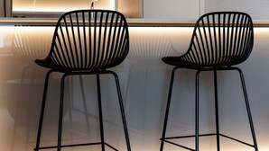 Två svarta stolar med en unik design, en modern vägg med en effektfull ljussättning och ett trägolv.