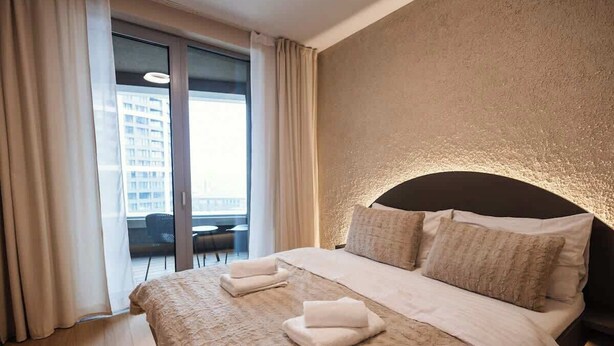 Ett hotellrum med en stor säng, en sänggavel, utsikt genom en skjutdörr och en balkong.