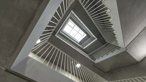 Una escalera de caracol con tragaluz en la parte superior, rodeada por una barandilla de metal con diseño geométrico.