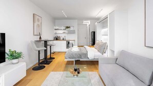 Una sala de estar moderna con un sofá, un comedor con sillas, una cocina con mostrador y un televisor.