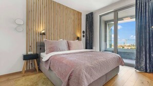 Ein modernes Schlafzimmer mit Bett, Nachttisch, Lampe und Blick durch eine Glastür.