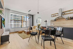 Un appartement moderne doté d’un coin repas, d’une cuisine et de grandes fenêtres donnant sur un panorama urbain.