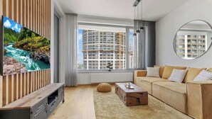Ein modernes Wohnzimmer mit einem Flachbildfernseher, einem Sofa, einem Couchtisch und einem großen Fenster mit Blick auf ein Bauprojekt.