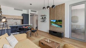 Ein modernes Wohnzimmer mit einer Couch, einem Couchtisch und einem Fernseher. Es gibt eine Küchenzeile mit einem Esstisch und Stühlen.