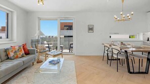 Een moderne woonkamer met een bank, salontafel en een eethoek met stoelen.
